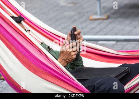 Persona sdraiata in un'amaca colorata guardando il suo telefono cellulare. Foto Stock