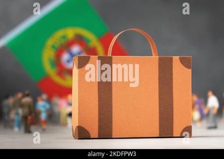 Valigia di cartone, personaggi di giocattoli di plastica e una bandiera su uno sfondo astratto, un concetto sul tema del trasferimento o dell'immigrazione in Portogallo Foto Stock