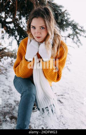 Teen bionda in un maglione giallo fuori in inverno. Una ragazza adolescente in una passeggiata in abiti invernali in una foresta innevata. Foto Stock