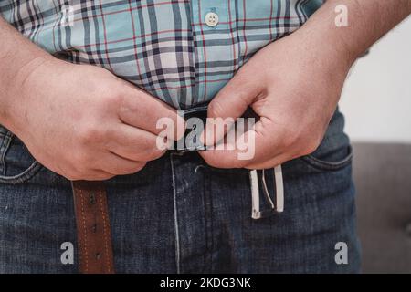 Primo piano delle mani di un uomo che indossa un paio di jeans blu e chiude la cintura (bottone). Foto Stock