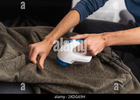 man rimuove le pillole di tessuto utilizzando un rasoio per pelucchi. Foto Stock