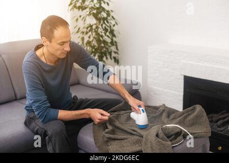 man rimuove le pillole di tessuto utilizzando un rasoio per pelucchi. Foto Stock