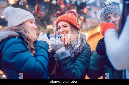 Gruppo di amici che bevono VIN brulé al freddo in un mercatino di Natale Foto Stock