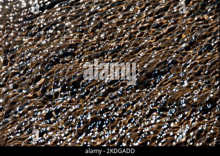 Sulla sabbia della spiaggia si formano ermetiche ondulazioni d'acqua che creano uno sfondo astratto Foto Stock