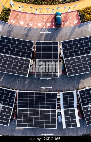 Vista aerea direttamente sopra auto elettriche parcheggio sotto pannelli solari su un parcheggio tetto pronto per la ricarica Foto Stock