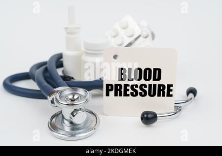 Concetto medico. Su una superficie bianca, farmaci, uno stetoscopio e carta da scrittura con il testo - pressione sanguigna Foto Stock