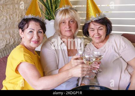 Donne anziane felici che indossano cappelli da festa bere vino insieme al ristorante . Foto Stock