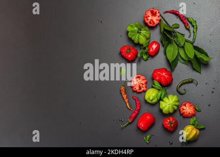 Pomodori verdi e rossi a coste, varietà americana o fiorentina. Verdure mature, peperoncino, foglie fresche di alloro. Luce tenebrosa, ombra scura, calcestruzzo di pietra Foto Stock