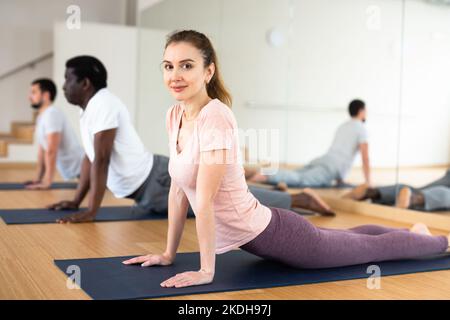 Donna che pratica il cobra posa con il gruppo in palestra Foto Stock