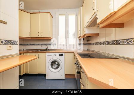 Cucina con armadi in legno color crema, piano di lavoro in legno e piastrelle con bordo Foto Stock