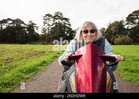 donna disabile in pensione su uno scooter da mobilità sorridente all'aperto Foto Stock