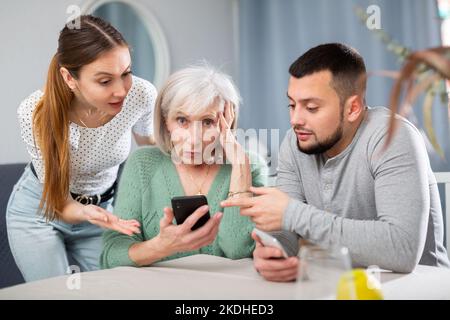 Giovane coppia che aiuta le donne anziane ad usare lo smartphone Foto Stock