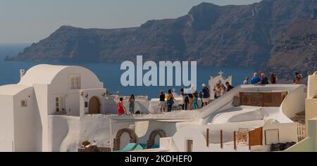 Oia, Santorini, Grecia. 2022. Turisti che scattano foto da alloggi Cliffside di fronte al mare Egeo a Oia sull'isola di Santorini, Grecia. Foto Stock