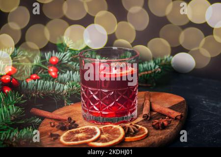 VIN brulé in un bicchiere su tagliere di legno con spezie, rametto di abete rosso e bokeh sullo sfondo, primo piano. Foto Stock
