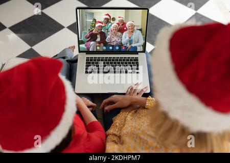 Madre e figlia diverse con cappelli di babbo natale che hanno videochiamata con amici diversi anziani felici Foto Stock