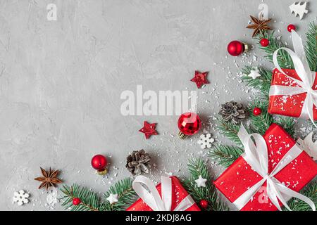 Composizione di Natale. Scatole regalo rosse, abete e decorazioni per le vacanze su sfondo grigio. Giacitura piatta. Layout. Vista dall'alto con spazio di copia Foto Stock