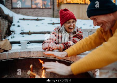 Coppia anziana seduta e riscaldamento insieme al caminetto all'aperto nella sera d'inverno. Foto Stock