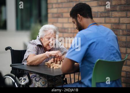 Caregiver giocare a scacchi con il suo cliente all'aperto al bar. Foto Stock