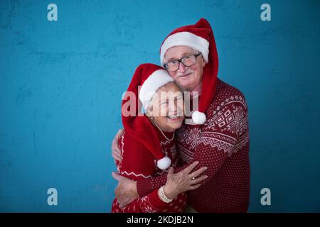 Ritratto di felice coppia anziana in maglioni di Natale abbracciando, riprese in studio. Foto Stock