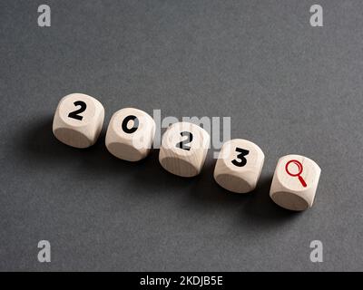 Alla ricerca di nuove tendenze e opportunità nel 2023. Cubi di legno con l'anno 2023 e una lente di ingrandimento icona. Foto Stock