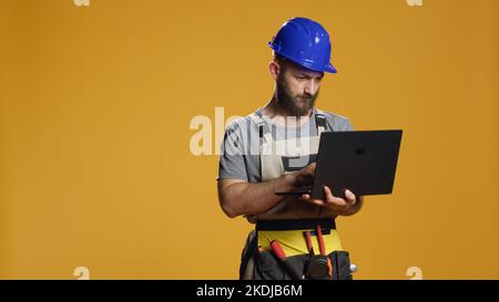 Ritratto di handyman che utilizza il computer portatile per trovare ispirazione per la costruzione e lavorare su un piano di ristrutturazione. Navigare in Internet su pc per eseguire misurazioni e processi di ingegneria in studio. Foto Stock