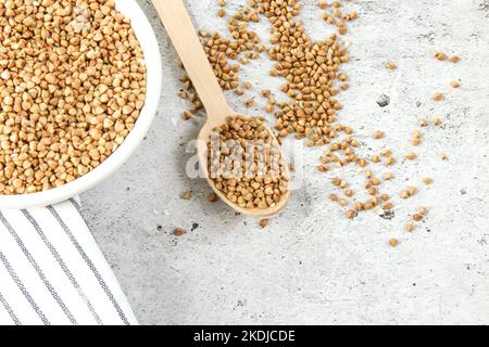 Grano saraceno in una ciotola bianca con cucchiaio di legno, grano saraceno crudo verde Foto Stock