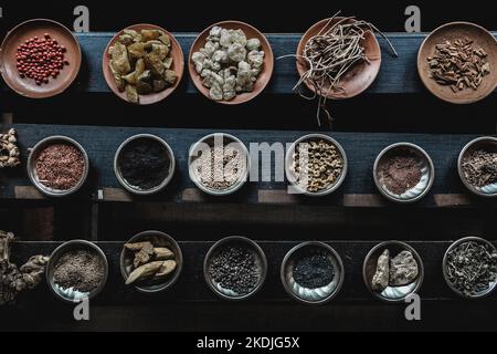 Varie spezie visualizzate su piccole piastre in ceramica e metallo su fondo in legno nero Foto Stock