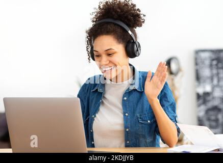 Felice afroamericana studentessa in cuffie utilizzando computer portatile con videochiamata Foto Stock