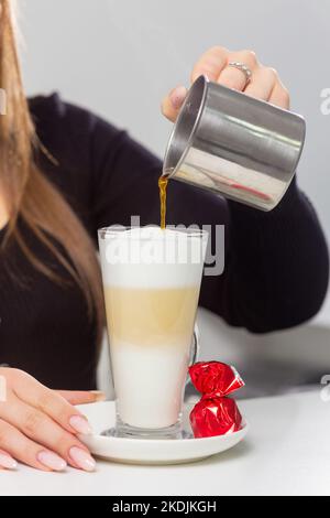 Barista girl versa il latte da una caraffa metallica in un bicchiere di caffè. Un accogliente caffè per incontrare gli amici. Foto leggera. Foto Stock