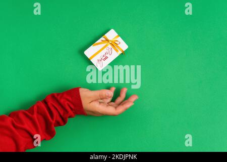 Mano femmina che tiene levitating modello della carta di indennità mockup, carta di credito della banca con nastro del regalo per lo shopping in linea isolato su fondo verde Foto Stock