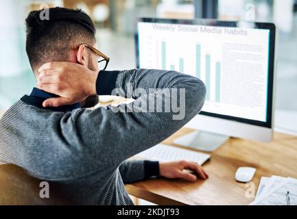 Sentendo la tensione e la tensione insinuarsi nel collo. Un giovane designer che soffre di dolore al collo mentre lavora alla sua scrivania. Foto Stock