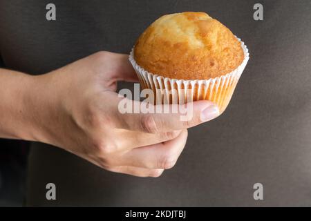 Mano femminile con gustoso cupcake sullo sfondo marrone Foto Stock