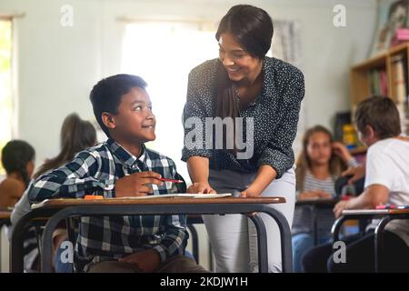 Capisci ora. Un giovane insegnante che aiuta i suoi studenti con i compiti a casa in classe. Foto Stock