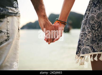 Ovunque è perfetto fintanto che sono stati a portata di mano. Primo piano di una giovane coppia che tiene le mani in spiaggia. Foto Stock