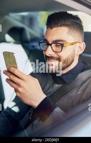 Fa le cose anche in viaggio. Un giovane designer che usa un cellulare in auto. Foto Stock