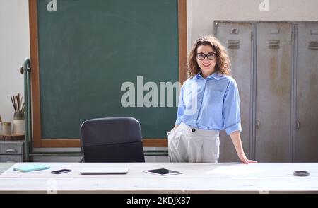 Giovane insegnante di scuola donna in piedi alla scrivania di fronte alla lavagna in classe. Foto Stock