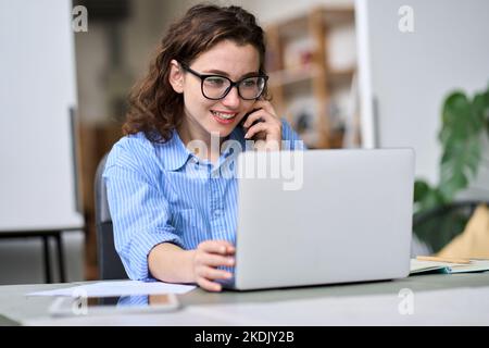 Giovane donna che parla al telefono utilizzando un computer portatile che lavora online. Foto Stock