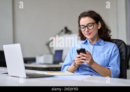 Giovane donna in viaggio d'affari che utilizza la seduta mobile alla scrivania in ufficio. Foto Stock