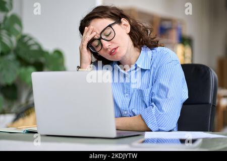 Giovane donna d'affari stanca che tocca la testa sensazione di emicrania emicrania utilizzando il notebook. Foto Stock
