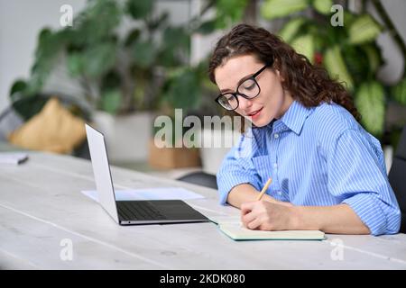 Giovane donna d'affari che scrive appunti lavorando alla scrivania con un computer portatile. Foto Stock