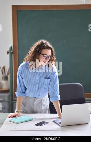 Giovane donna insegnante di scuola, tutor online in piedi alla scrivania insegnamento a distanza classe. Foto Stock