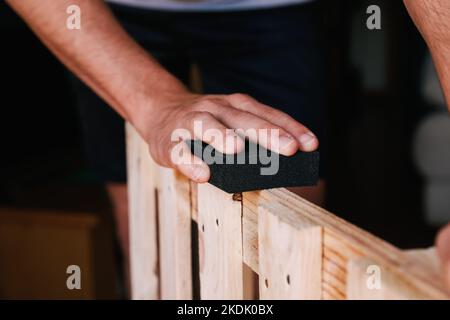 Mano dell'uomo irriconoscibile levigare un pallet. Ristrutturazione domestica Foto Stock