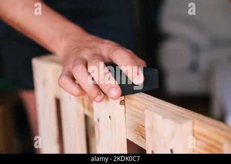 Mano dell'uomo irriconoscibile levigare un pallet. Ristrutturazione domestica Foto Stock