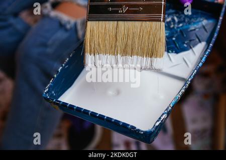 Primo piano mani irriconoscibili della donna con guanti viola che prendono la vernice con un pennello in un vassoio riforme Foto Stock