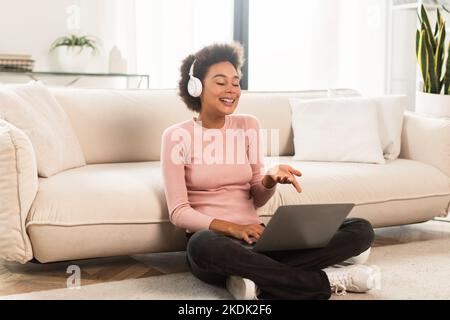 Allegro millenario afroamericana donna in cuffie wireless ha videochiamata sul portatile, gesturing Foto Stock