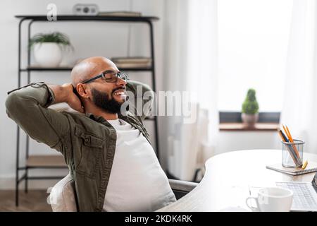 Uomo freelance maturo positivo che si appoggia sulla sedia, si rilassa dopo un lavoro di successo, si siede al tavolo in ufficio, spazio libero Foto Stock