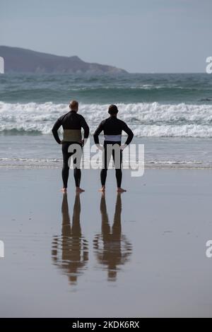 Due surfisti che indossano mute nere che si affacciano sul mare su Una spiaggia di Lanzada, o Grove Foto Stock