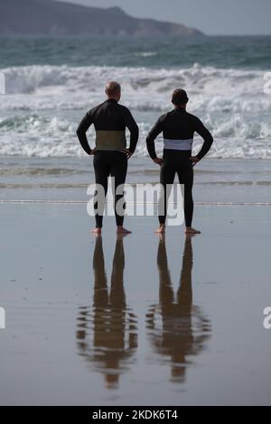 Due surfisti che indossano mute nere che si affacciano sul mare su Una spiaggia di Lanzada, o Grove Foto Stock