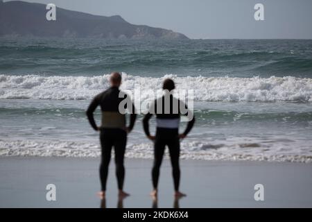 Due surfisti che indossano mute nere che si affacciano sul mare su Una spiaggia di Lanzada, o Grove Foto Stock