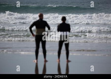 Due surfisti che indossano mute nere che si affacciano sul mare su Una spiaggia di Lanzada, o Grove Foto Stock